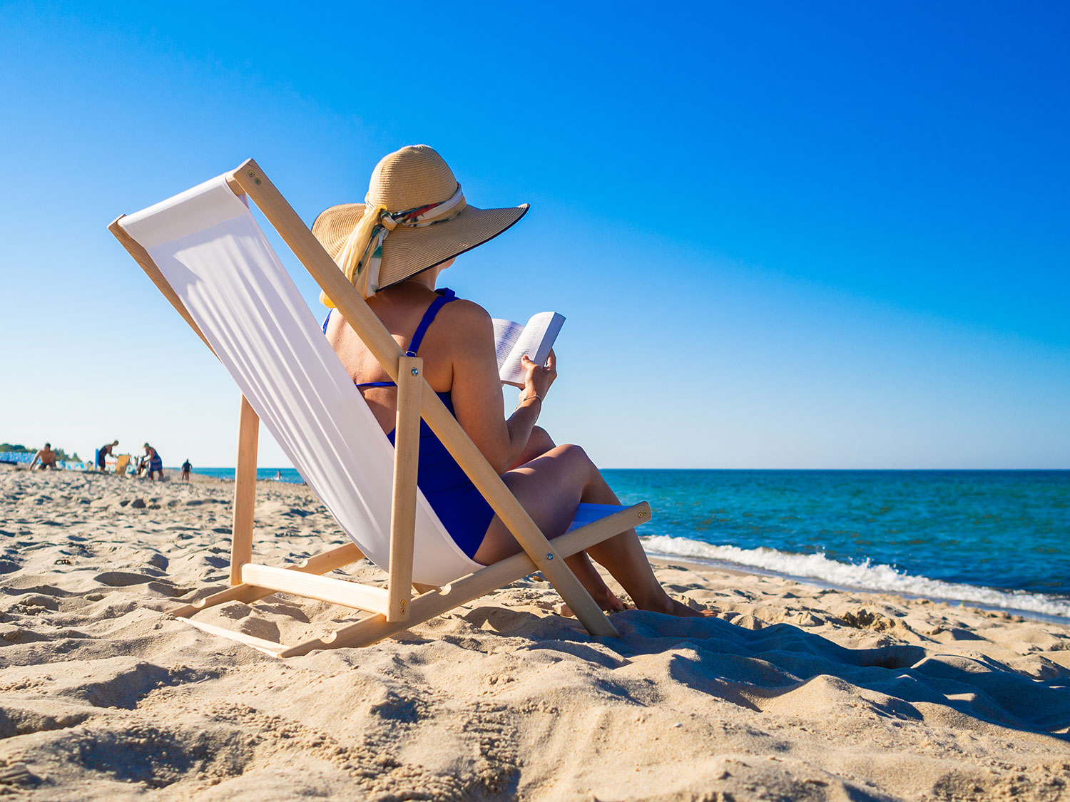 Plaża nad Morzem Bałtyckim: kobieta w kapeluszu przeciwsłonecznym czytająca książkę na leżaku